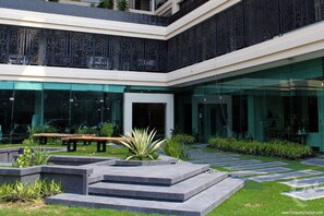 A modern building with a glass facade, outdoor seating, and a landscaped courtyard.