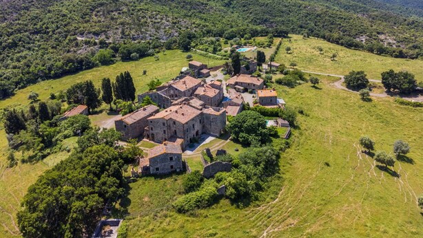 Un pueblo histórico de piedra con arquitectura tradicional, rodeado de exuberantes campos verdes y colinas.
