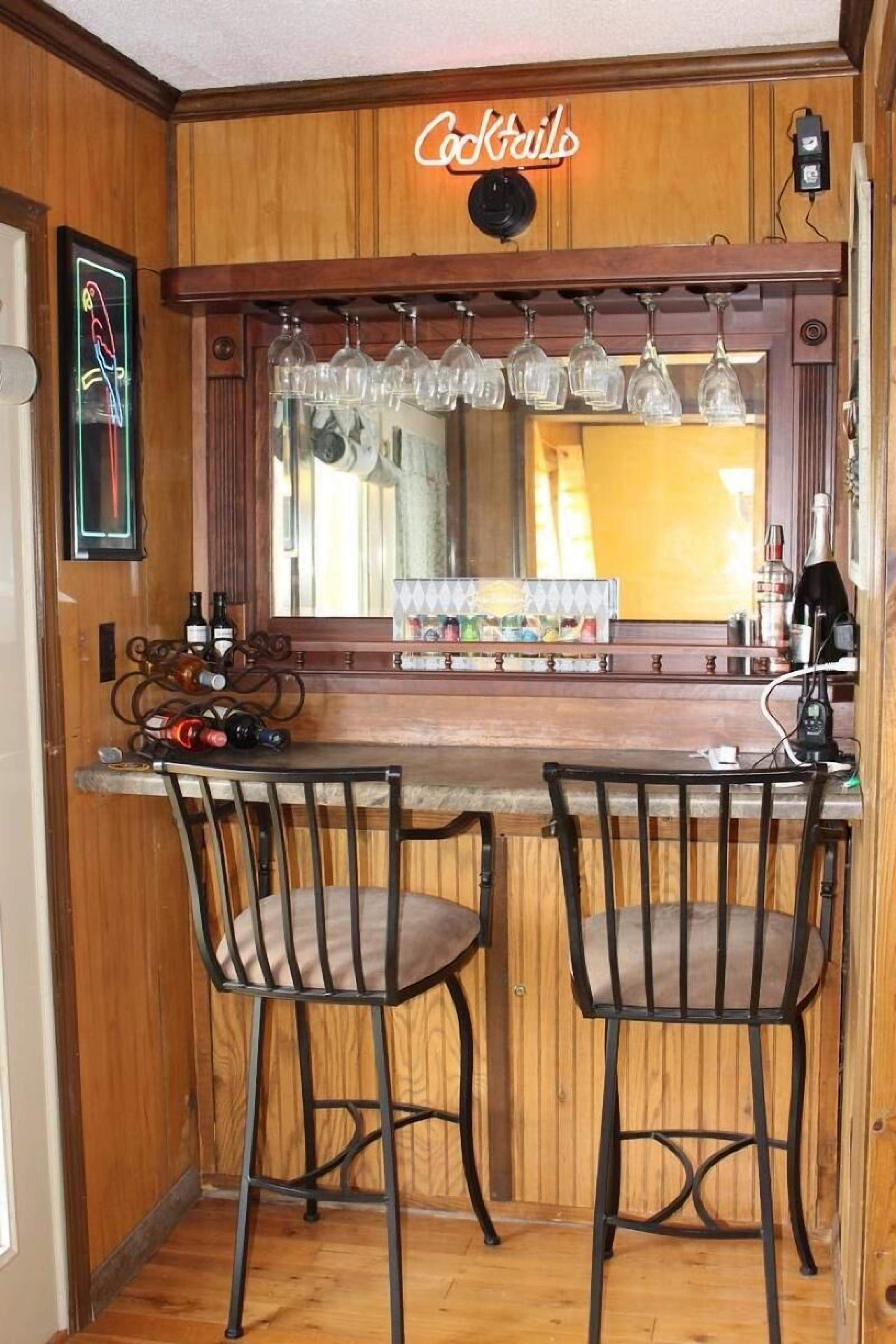 Zona de bar con dos taburetes metálicos, una barra de madera y un letrero de neón que dice "Cocktails".