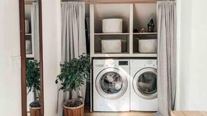A compact laundry area with a washing machine and dryer, a potted plant, and storage shelves.
