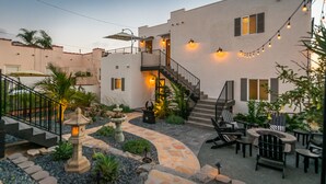 A courtyard with a stone pathway, outdoor seating, a staircase, and string lights.