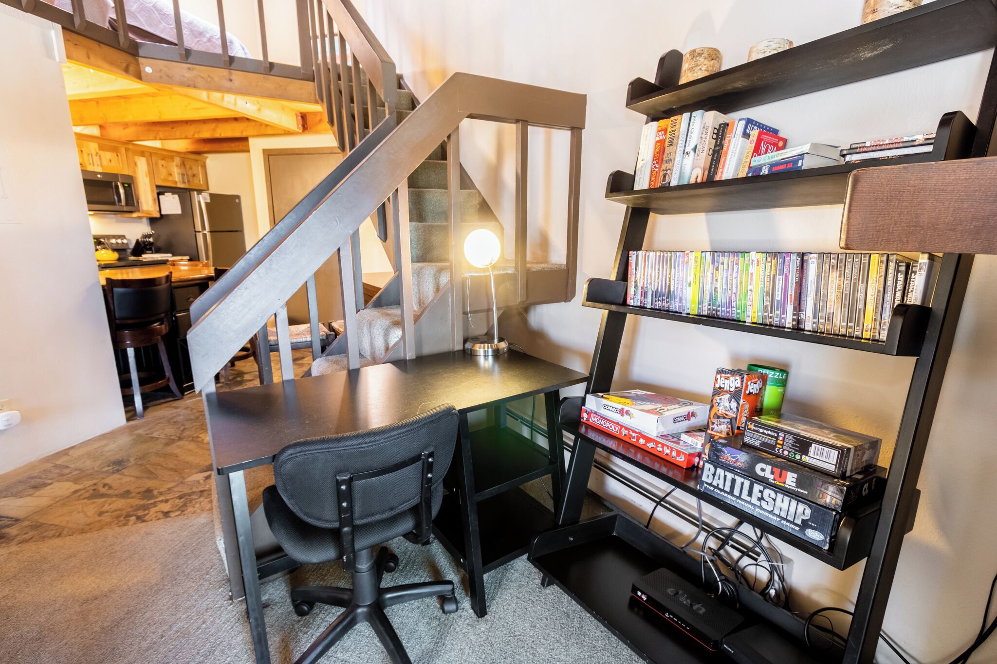 A home office with a desk, chair, and a bookshelf filled with books and games.