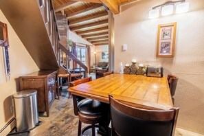 A dining area with a large wooden table, chairs, and a staircase leading to another room. - Treehouse #305, Building D by Summit County Mountain Retreats (Silverthorne)