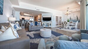 A spacious living room with a grey sofa, a round coffee table, and a dining area with white chairs. - Phoenix West ~ Three Bedroom ~ Low Floor! (Orange Beach)