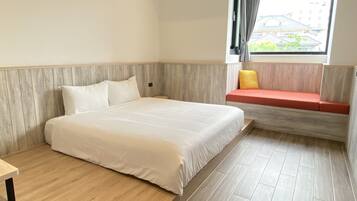 A hotel room with a bed, a small table, a window with curtains, and a bench with cushions.