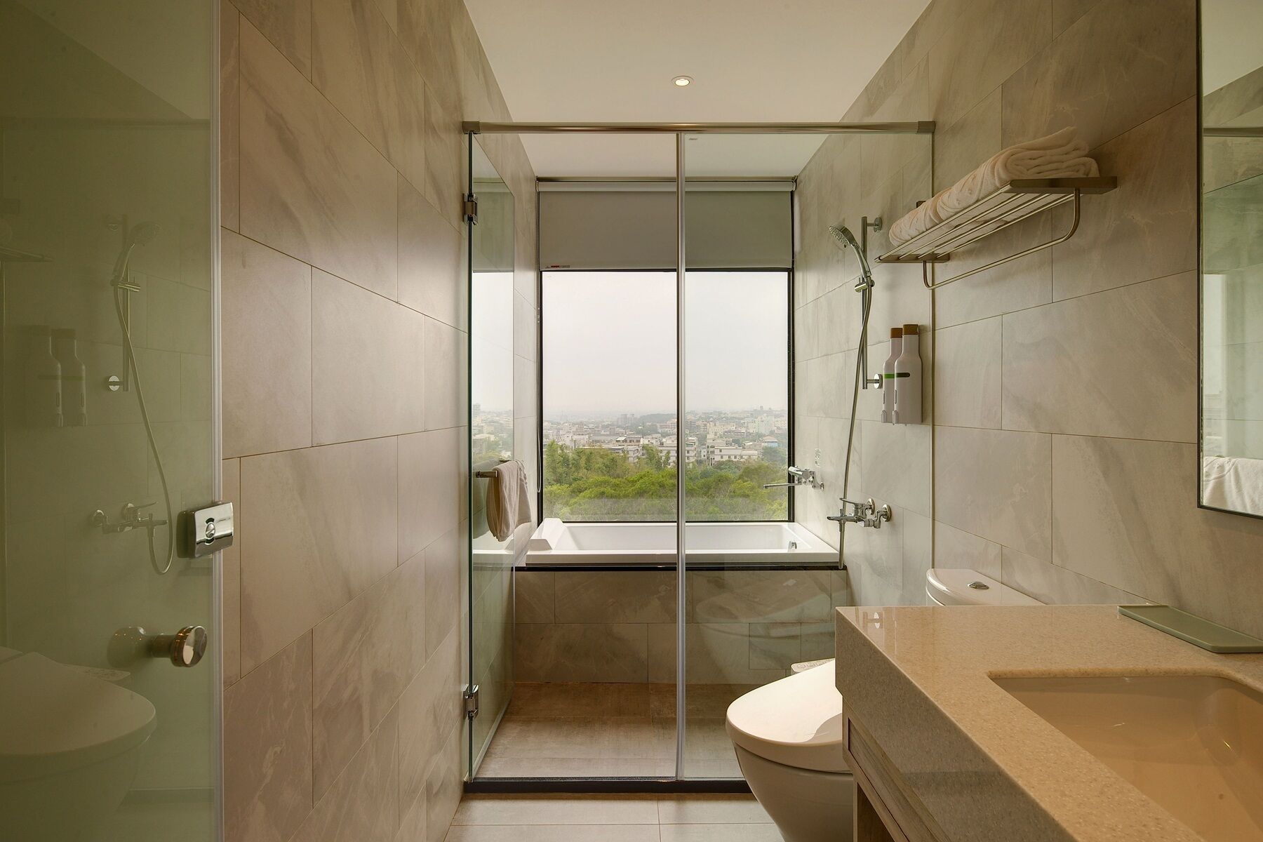 A modern bathroom with a glass-enclosed shower, a large mirror, and a view of a cityscape.