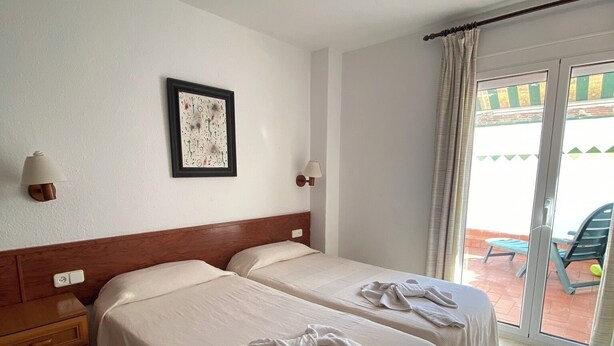 Hotelkamer met twee bedden, een houten hoofdeinde, een ingelijst schilderij aan de muur en een glazen schuifdeur naar een buitenruimte.