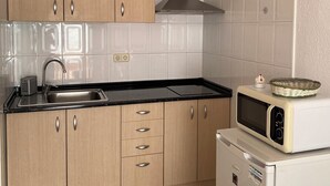 Een keuken met houten kastjes, een roestvrijstalen spoelbak, een magnetron en een inbouw afzuigkap.