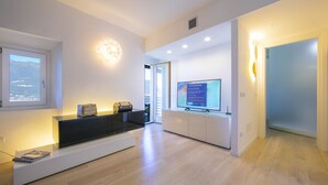 Een moderne woonkamer met een inbouwkast, een grote flatscreen televisie en een zithoek met een lange bank.