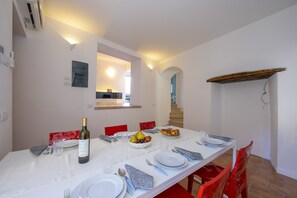 A dining area with a white table set for four, including plates, cutlery, and a bottle of wine. A fruit bowl and a plate of croissants are also visible.