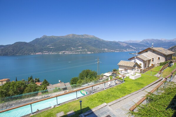 A lakeside property with a swimming pool, a wooden deck, and a view of the lake and mountains.