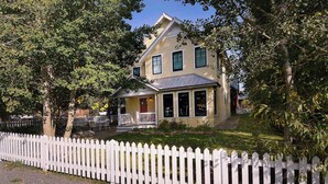 A two-story house with a porch, a picket fence, and a well-maintained lawn.