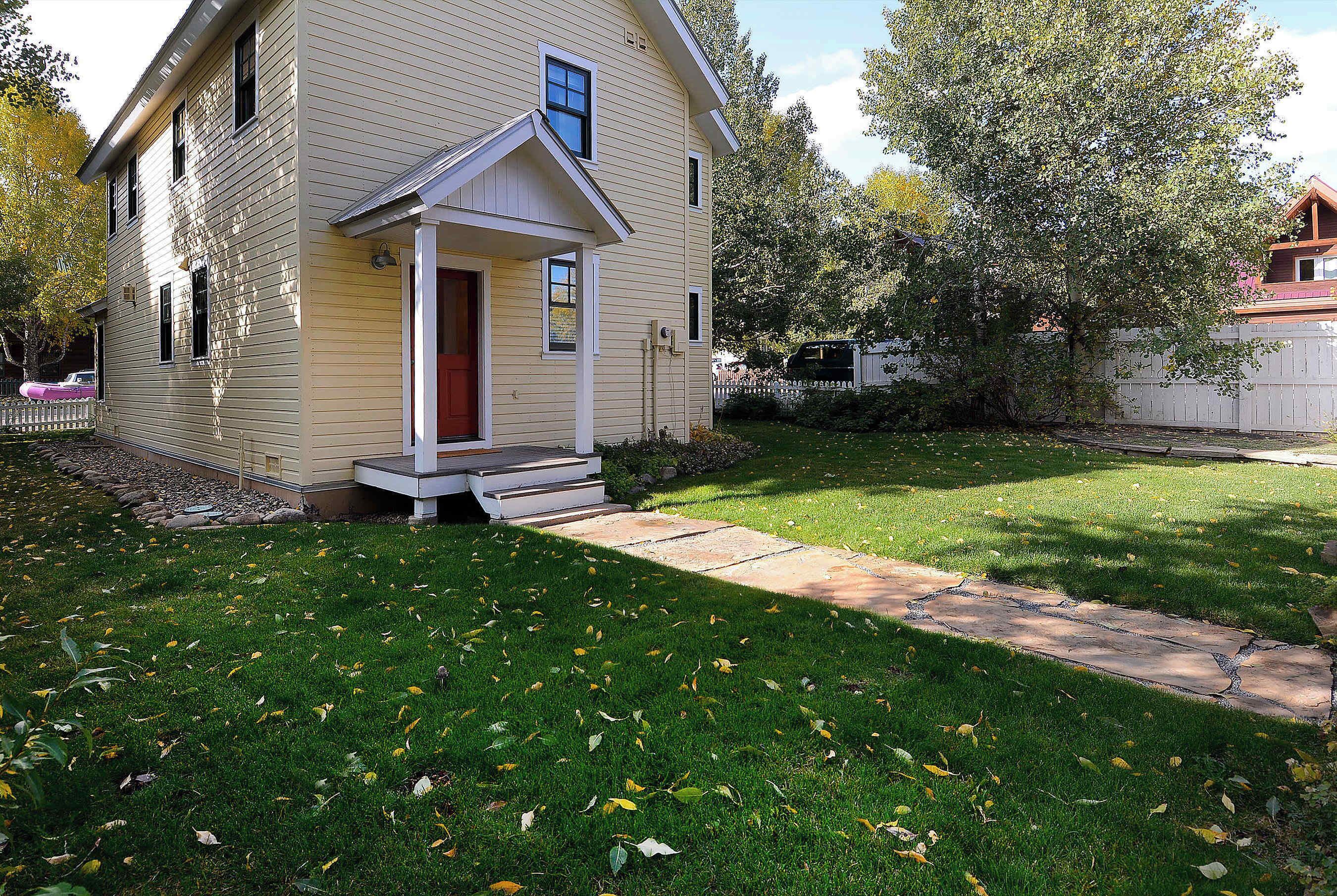 A two-story house with a front porch, a small front yard, and a wooden fence.