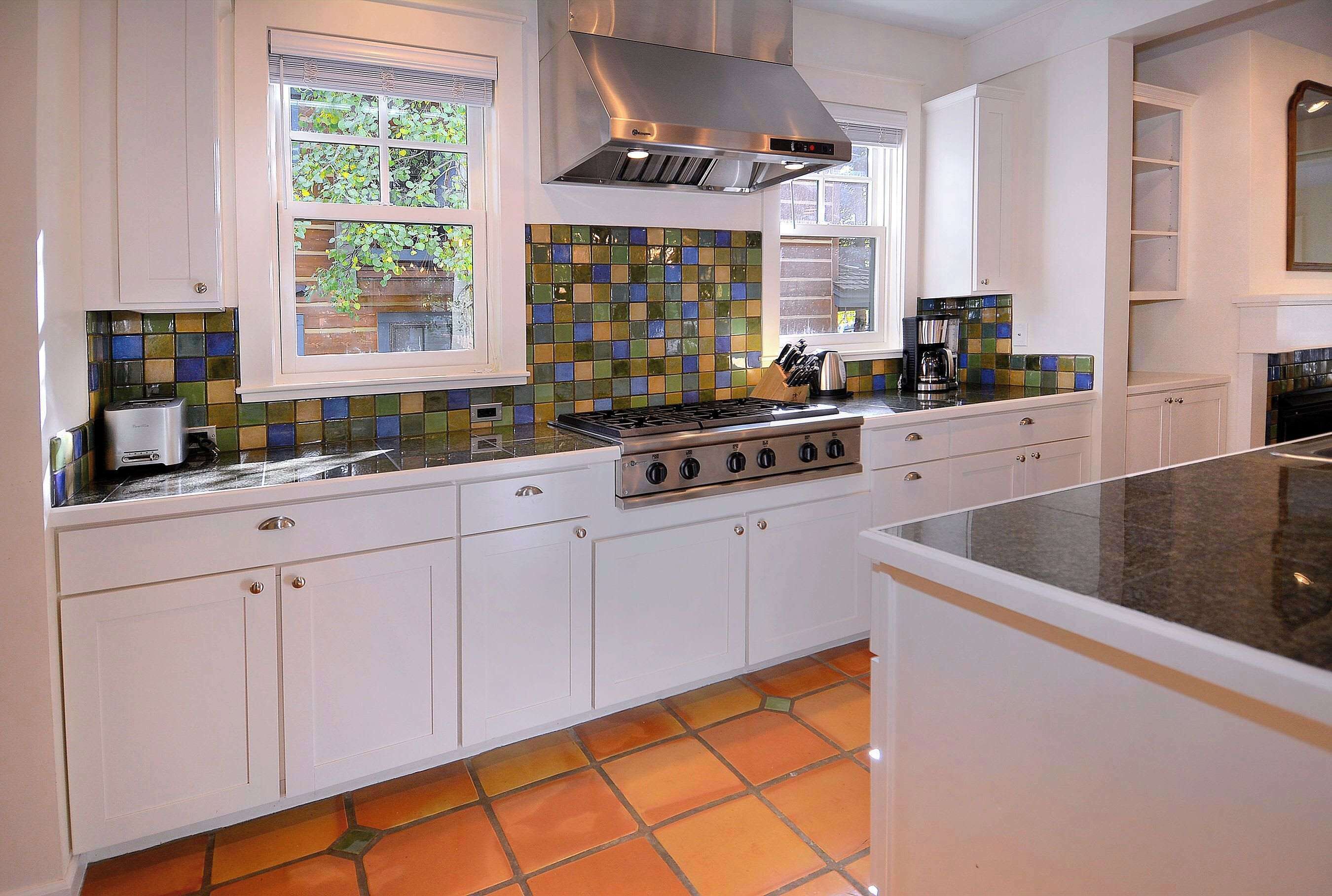 A kitchen with white cabinets, a gas stove, a stainless steel range hood, and a window with a view of greenery.