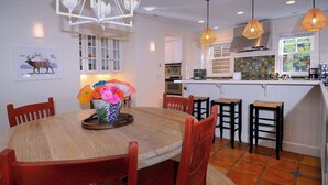 A dining area with a wooden table and chairs, a vase with flowers, and a kitchen in the background.
