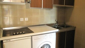 Cocina compacta con lavadora y secadora integradas, electrodomésticos de acero inoxidable y un lavamanos pequeño.
