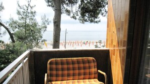 Un balcón con un sofá a cuadros, una pequeña mesa con un farol y vista a la playa con boyas naranjas.