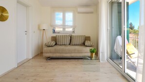 Una sala de estar con un sofá, una mesa de centro de vidrio, una lámpara y vistas a través de un ventanal corredero.