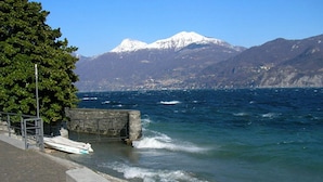 A coastal scene with a bench, a boat, and a mountain in the background. - Residenza Menaggio - Glicine (Menaggio)