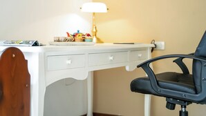 Un escritorio blanco con una lámpara, una silla y una mesita con objetos encima.