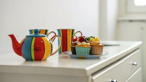 Una tetera colorida y dos tazas a rayas sobre una mesa blanca.