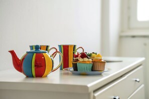 Une table blanche avec une théière colorée, une tasse à rayures et une assiette remplie de petits gâteaux.
