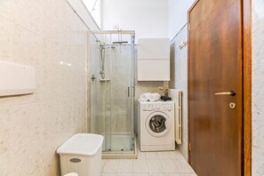 Ett litet badrum med en dusch som är avskärmad med glasväggar, en tvättmaskin och en dörr av trä.