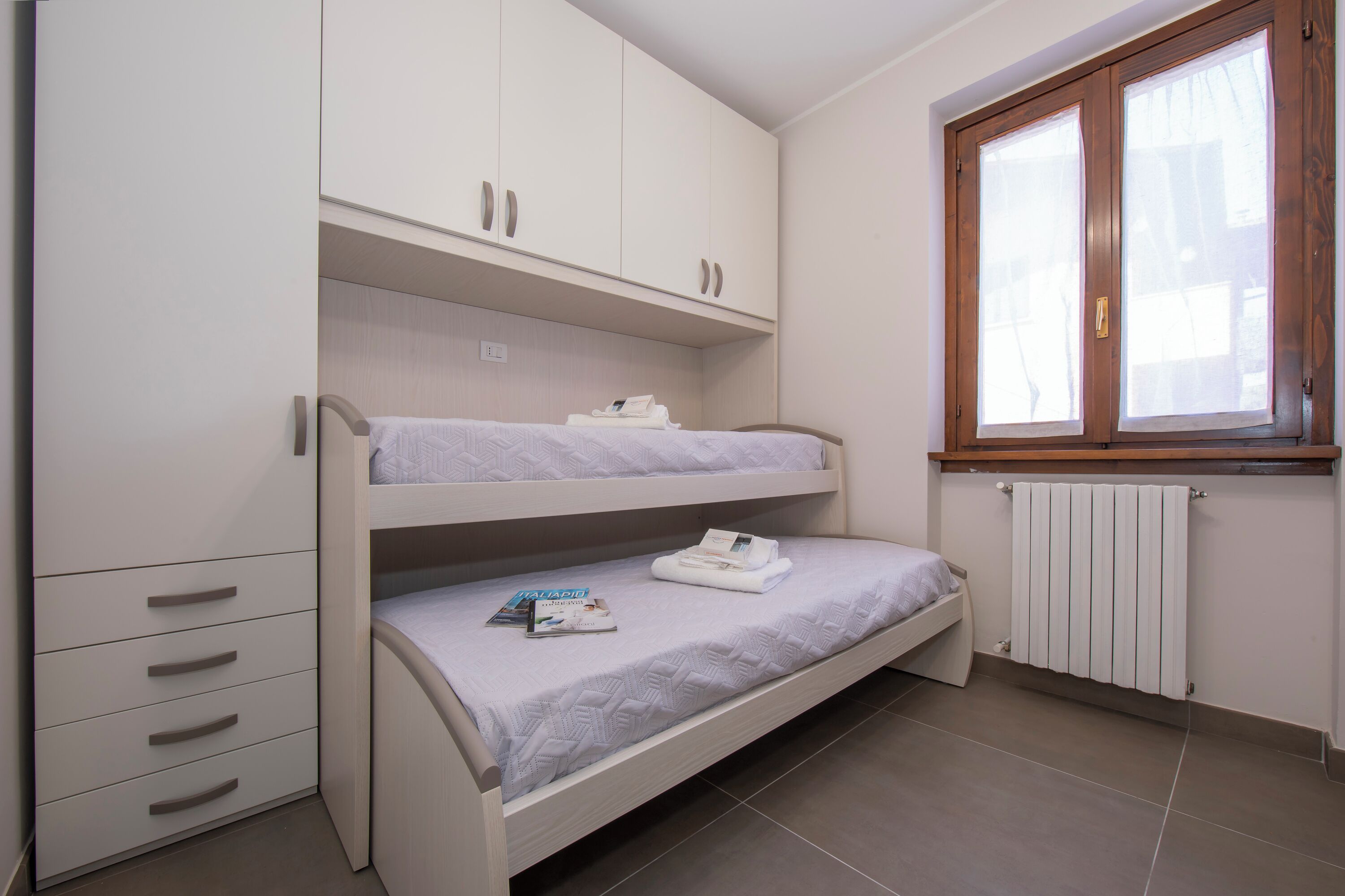 A bunk bed room with a white wardrobe, a radiator, and a window.