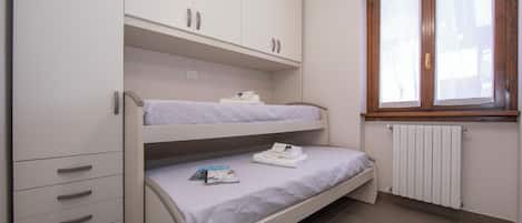 Habitación con literas, un armario blanco, un radiador y una ventana.