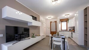A modern kitchen with white cabinetry, a dining area with a table and chairs, a built-in TV, and a ceiling light fixture. - Menaggio Palphi (Menaggio)