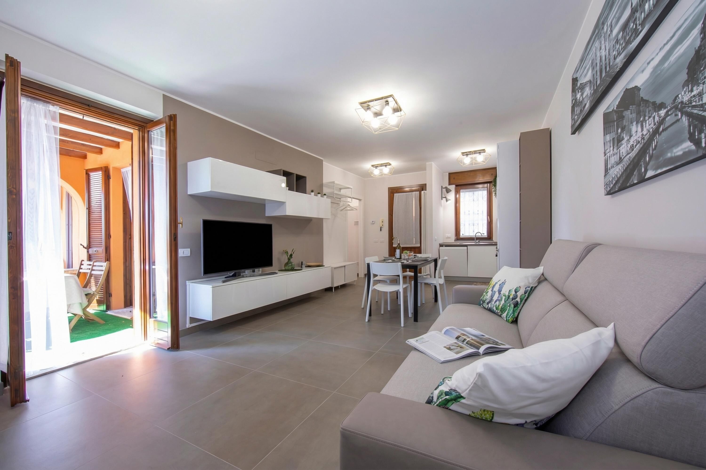 A modern living room with a sofa, TV, dining area, and a kitchen in the background.