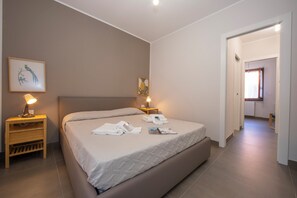 Ett hotellrum med en säng, sängbord med lampor, en inramad tavla på väggen och en dörr som leder till ett annat rum.