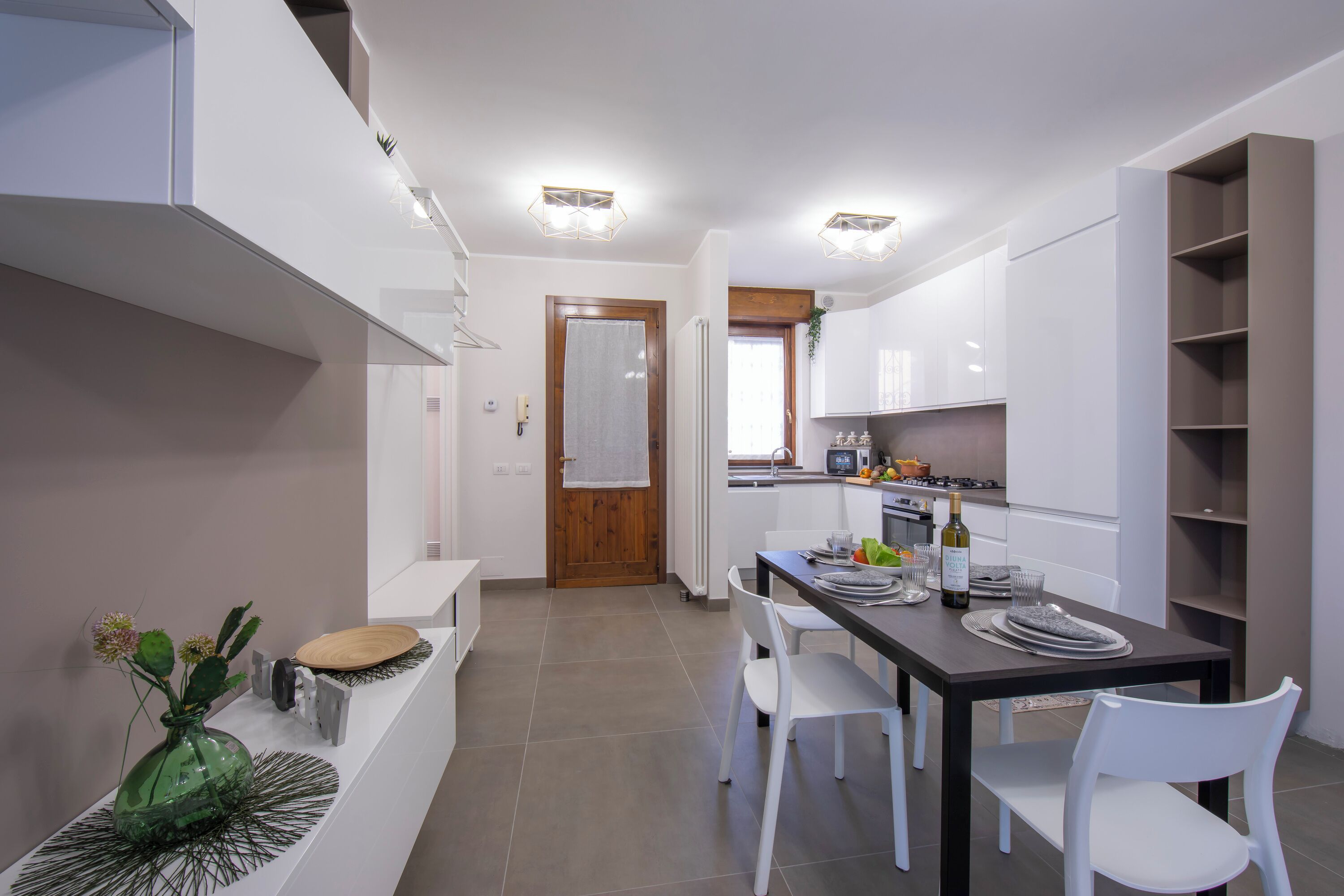 A modern kitchen with white cabinets, a dining table with chairs, and a small side table with a vase.