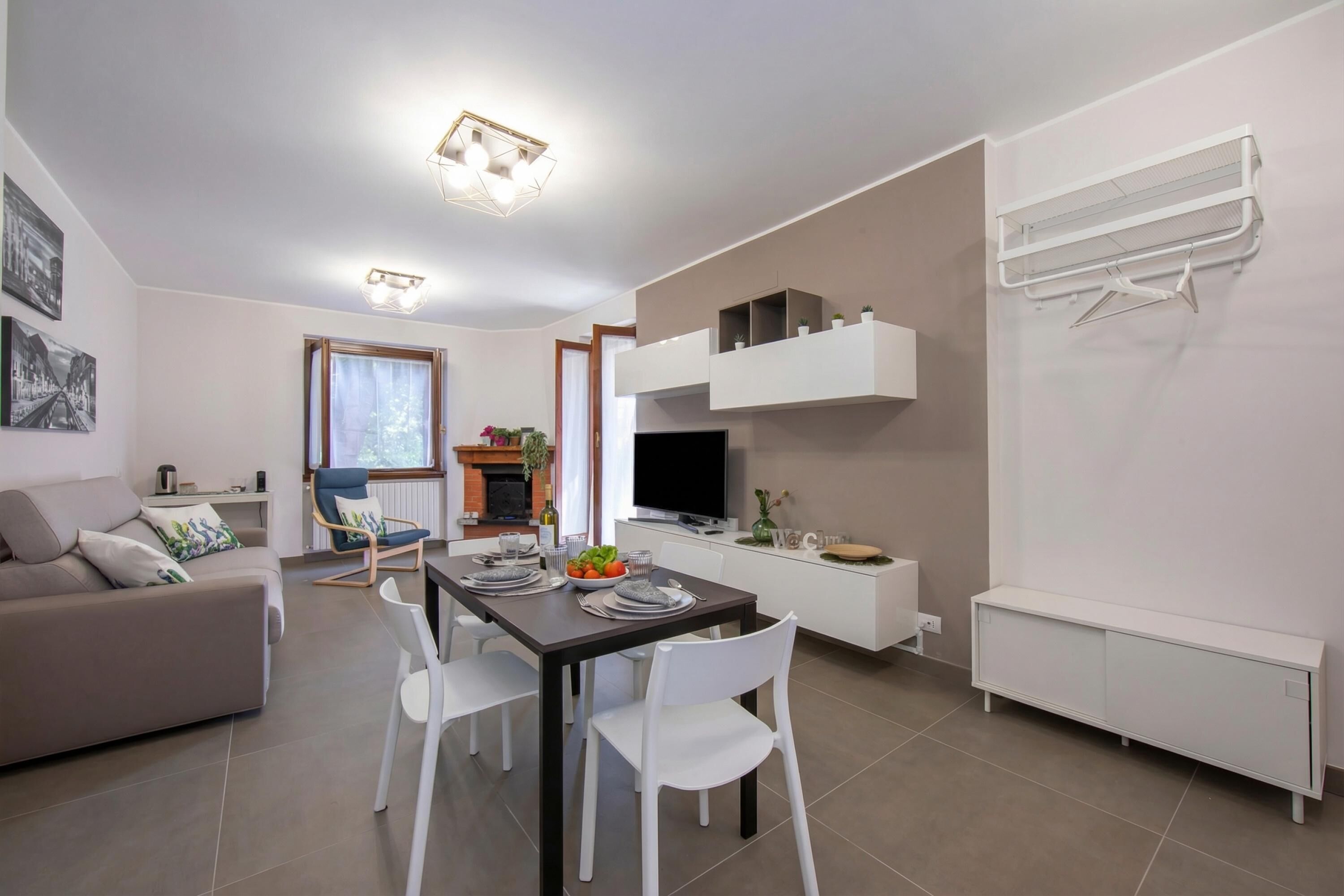 A modern living room with a sofa, dining table, and chairs. There is a TV, a fireplace, and a white radiator.