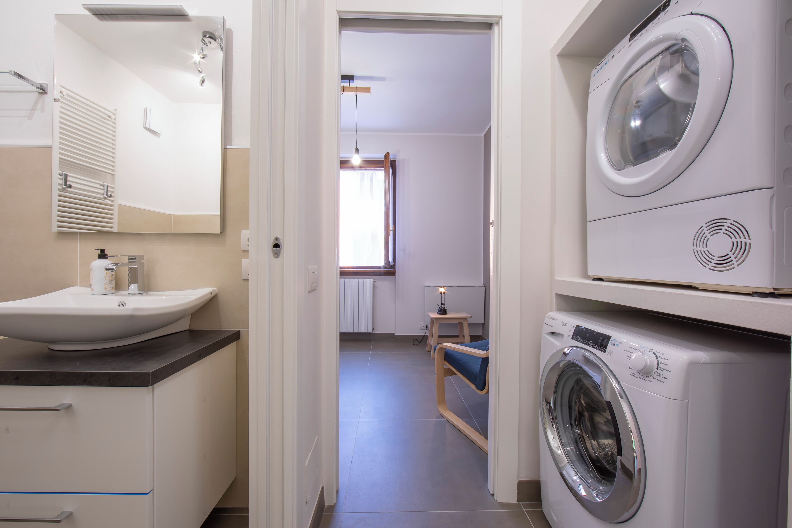 Ein kleines Badezimmer mit Waschbecken, Spiegel und übereinander gestapelten Waschmaschinen.