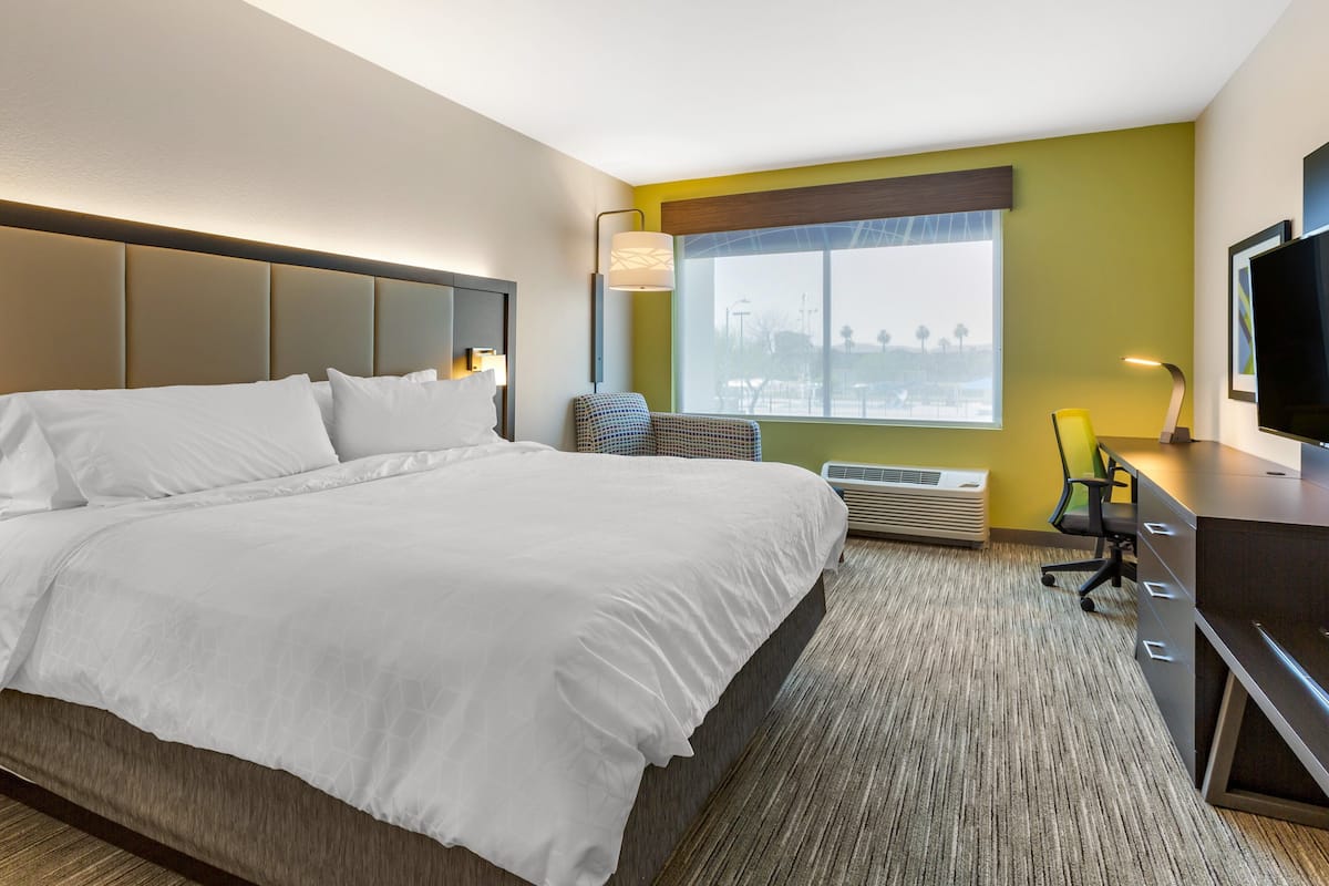 A hotel room with a large bed, a desk with a chair, a television, and a window with a view.