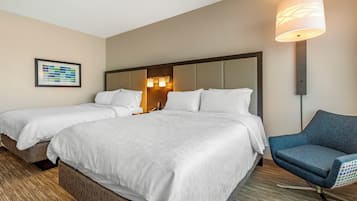 A hotel room with two beds, a blue armchair, a framed picture on the wall, and a lamp.
