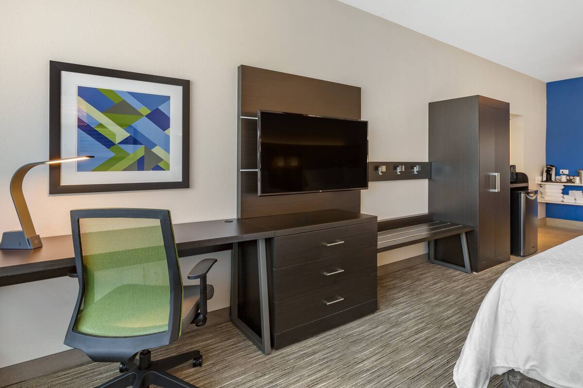 A hotel room with a desk, chair, TV, wardrobe, and bed.