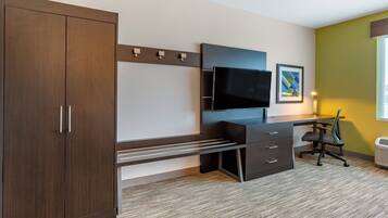 Quarto de hotel com guarda-roupa de madeira, escrivaninha com televisão de tela plana, uma cadeira e um quadro na parede.
