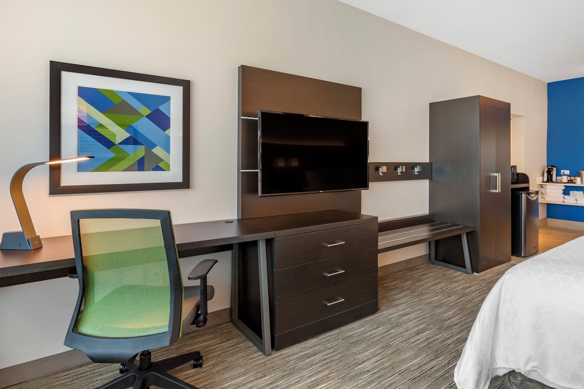 Ein Hotelzimmer mit Schreibtisch, Stuhl, Fernseher, Kleiderschrank und einem Bett.