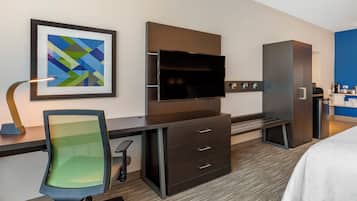 A hotel room with a desk, chair, television, wardrobe, and a bed.
