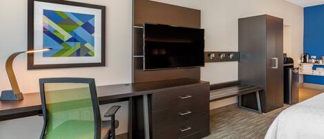 A hotel room with a desk, chair, television, wardrobe, and a bed.