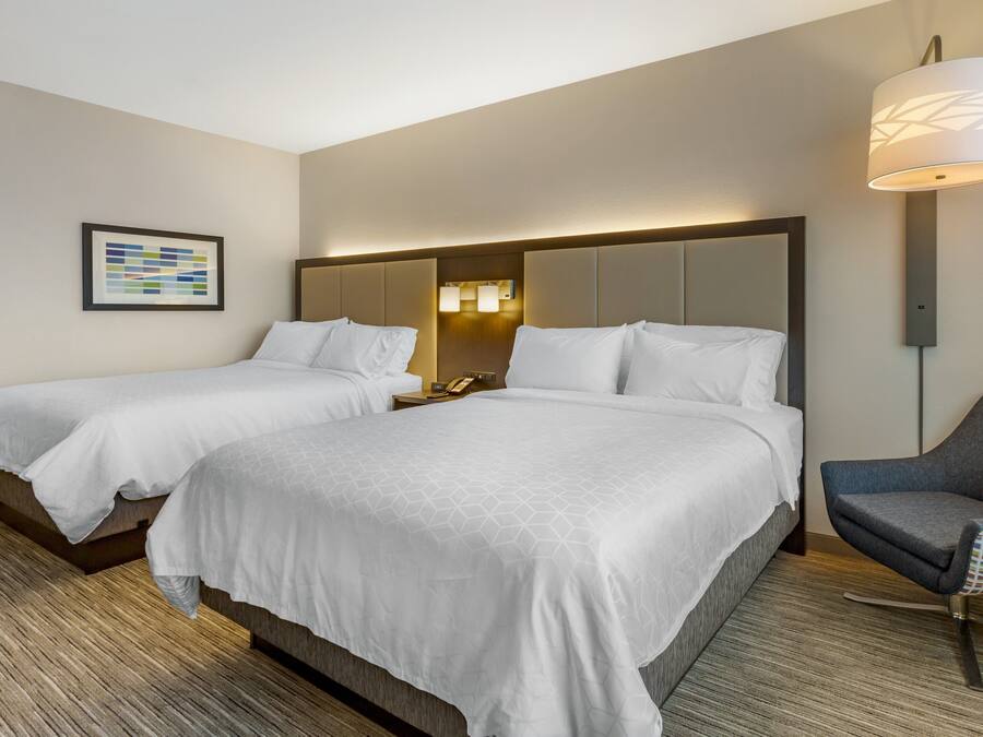Habitación de hotel con dos camas, un escritorio, una silla, una lámpara y un cuadro en la pared.