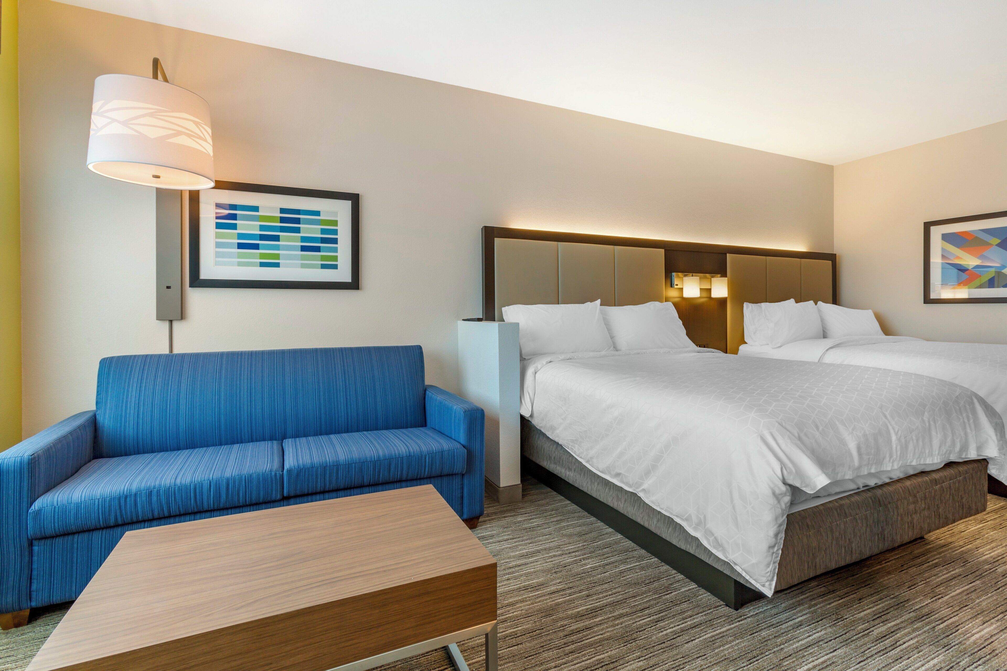 Une chambre d’hôtel avec un lit, un canapé, une petite table et deux lampes fixées au mur.