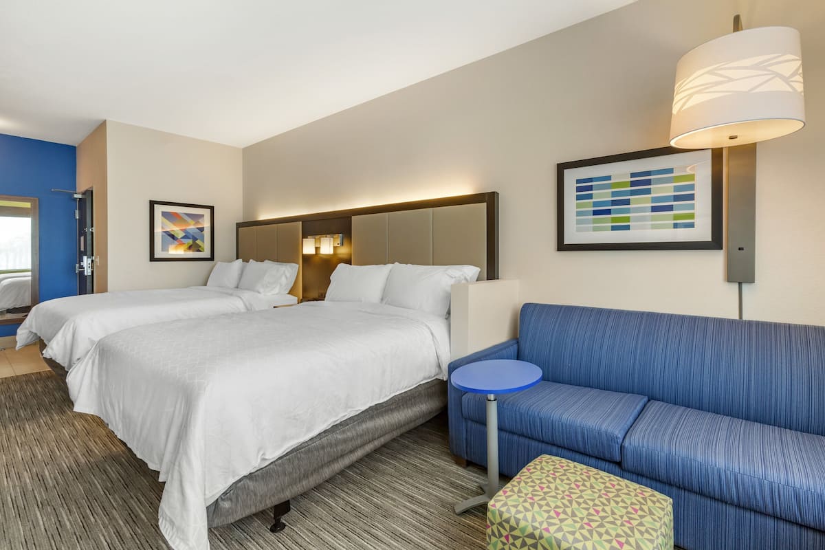 A hotel room with two beds, a blue sofa, a small round table, and a patterned ottoman.