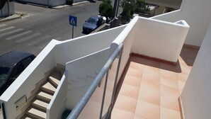 Ein Wohngebäude mit einer Treppe, die zu einem Balkon führt, einem blauen Fußgängerüberweg-Schild und geparkten Autos in der Straße.