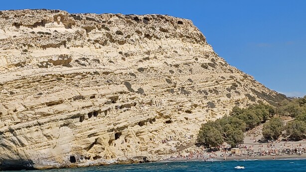 Une falaise côtière aux formations rocheuses stratifiées, avec une plage au premier plan.