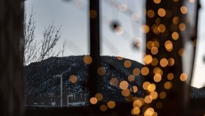En vy genom ett fönster med suddiga ljus i förgrunden, ett snötäckt landskap och en byggnad i bakgrunden.