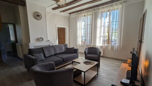 Un salon comprenant un canapé, un fauteuil, une table basse et un téléviseur posé sur un meuble en bois.