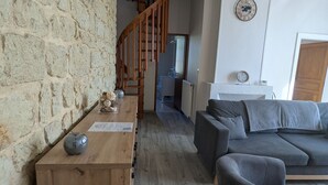 Un salon chaleureux avec un mur en pierre, des meubles en bois, un canapé gris et une table en bois agrémentée d’objets décoratifs.